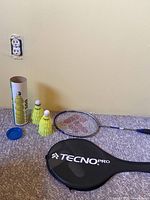 Full set laid on carpet: Tecno Pro racket, case, tube of yellow birdies with 2 birdies outside the tube