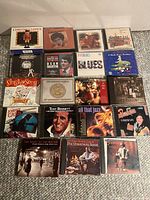 Photo showing all 19 CD jewel cases laid out on carpet, titles visible including various blues, jazz, and Christmas music collections.