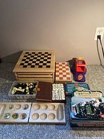 Wide shot of board games lot featuring wooden chess chest, chess pieces, domino sets, travel game boards, and UNO card dispenser machine