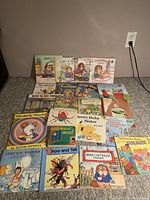 All 20 children's books arranged on carpet floor, showing illustrated front covers of titles including spot series, Franklin, Berenstain Bears, Mercer Mayer, Robert Munsch and classic stories like Where the Wild Things Are and Goodnight Moon.