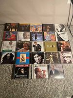 Top-down photo showing 23 CDs arranged on floor in 5 rows (5, 5, 5, 5, 3). Album covers visible with various classic music artists.