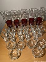 Front-facing photo showing arrangement of the 5 milkshake glasses, 5 red cups, 17 shot glasses, and 6 bubble whiskey glasses on a wooden surface.