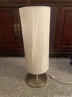 Full view of Ikea lamp showing textured cylindrical white shade and stainless steel round base on carpeted floor.