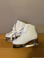 Pair of white kid's figure skates with laces, showing side profile of the left and right skate.