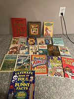 Photo showing 22 kid's books including joke books, fact books, and puzzle books spread on carpeted floor.