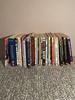 Photo of 20 books arranged standing next to each other showing spines and front covers from some titles, illustrating the whole collection to be sold.