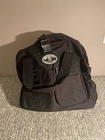 Front view of black Locomotor travel bag showing multiple zippered compartments and shoulder straps