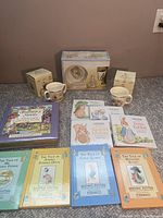 Wide shot of the entire Peter Rabbit collection showing the boxed Wedgwood bowl and cup, two boxed Royal Doulton mugs, and eight Beatrix Potter storybooks in a variety of colors.