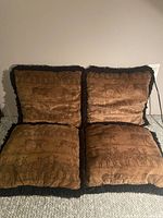 Photo showing set of four square throw pillows with brown safari animal prints including zebras and giraffes, black fringe border visible.