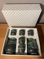 Top-down view of the sake set inside a white box with molded compartments showing two sake bottles and five cups arranged neatly.