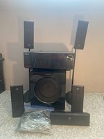 Samsung surround sound system components, including five speakers, subwoofer, receiver, and wires, arranged on carpet.
