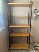 Full view of a wooden and metal shelf on wheels with five shelves, black metal frame, and caster wheels.