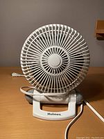 Front view of compact white Holmes tabletop fan showing fan blades enclosed in protective grille and electric power cord.
