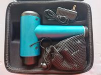 Photo of the blue electric handheld massage tool inside a case with the charger and carrying pouch.