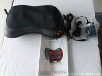 Shiatsu massager pillow shown on white surface with power adapter and user manual.