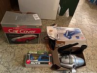 Motomaster car cover box, B&D Dirtbuster and other car vacuums in original boxes on basement floor