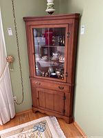 Front view of Krug wooden corner cabinet showing upper glass door and lower wooden door.