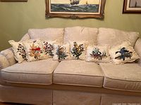 Full view of eight decorative cushions displayed on beige patterned sofa showing different embroidered bird motifs and lace trim edges.