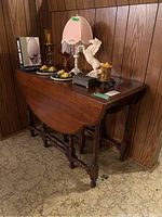 Wood gate-leg table with drop leaves closed, showing table in compact form with items on top including a lamp and decorative items.