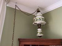 Image showing the entire hanging lamp suspended from a ceiling chain against a green wall background, displaying the floral glass pattern and metal fittings.