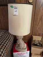 Full view of the lamp showing the beige fabric shade and ceramic foo dog base on a cardboard box.