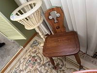 Photo of wooden cream-colored plant stand and brown wooden chair side by side on a rug near window and baseboard heater.