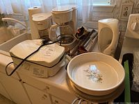 Kitchen counter with waffle maker, two coffee makers, electric kettle, and other kitchen items.