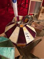 Overall view of stained glass lamp shade laid on floor with visible electrical mounting plate and wiring. Shade is octagonal with alternating amber, ivory, and burgundy stained glass panels.