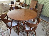 Round wooden table with 6 cushioned chairs arranged around it, showing condition and style.