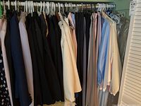 Image showing a rack of women's suits, dress pants, and blouses hanging side by side. Colors include black, beige, pink, blue, and gray. All garments appear to be in size range 10-12.