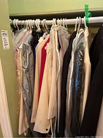 Photo shows a rack with assorted women's clothing including blazers, pants, and blouses in sizes 10-12 in various neutral colors such as beige, cream, black, and gray.