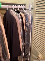 Photo of seven coats and jackets hanging on pink plastic hangers on a black rail, some covered with clear garment bags. Colors range from black, brown to beige.