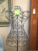 Close view of metal wire decorative dress form with ornate scrollwork, showing shape and base stand.