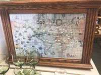 Showing the full front view of the Howard Miller world clock with wooden frame, vintage map and time zone indicators.