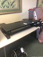 Black laminate standing desk top with Ivation branding, adjustable frame, keyboard tray visible, resting on a table.