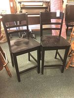 Pair of black painted wood ladder back bar height chairs side by side, showing overall condition; one in better condition, the other with chipped paint.