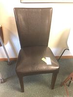 Single dark brown faux leather dining chair with a slightly curved high back and wooden legs.