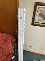 Eight white PVC pipes bundled together with clear plastic wrap leaning against a wall near a red patterned chair. Pipes have multiple round holes spaced along their length with some blue end caps visible.