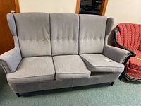 Front view of the gray fabric high back sofa showing three seat cushions, with one cushion slightly displaced, highlighting the cushion placement and fabric condition.