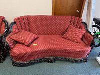 Front view of red upholstered sofa with carved dark wooden frame and two throw pillows on seat.