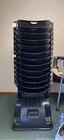 Full front view of 13 black stacking chairs neatly stacked on rolling base, showing perforated hard plastic seats and mesh backs.