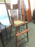 Full view of vintage wooden high chair with cane seat and carved press back, showing overall structure and condition including armrests and footrests.