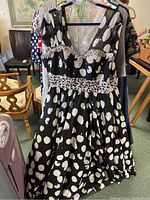 Photo showing the front side of a black dress with white abstract polka dots and sequin embellishments on the neckline and midsection.