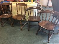 Four wooden chairs on carpet, two standard spindle back chairs and two round back chairs with armrests, all show wear.