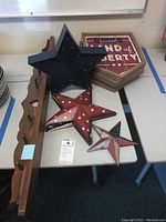 Photo of wood hat rack with nine pegs and decorative heart cut-out alongside a large black lighted star, medium red star, and two patriotic plaques.