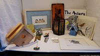 Full lot overview showing framed picture, candle holder, birdhouses, prints, coloring book, chimes and napkin holder