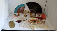 Full lot view showing multiple fans, brass candy dish, Hungarian crest plaque, candle holders, and additional decorative items.