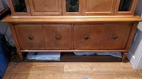 Front view of wooden buffet showing four doors with metal ring handles and tapered legs on hardwood floor.