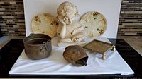 Bust sculpture, brass pot, cow bell, decorative plates and metal stand with tray on table showing the entire lot