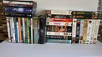 Photo showing two rows of DVDs and VHS tapes with visible titles including Band of Brothers series, Pink Panther, Planet Earth, The Blue Planet, Harry Potter VHS, Beaches, Analyze This and That VHS, and several movie titles on VHS.